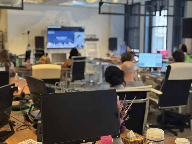 Employees working together in an open office during a team meeting, with laptops and shared screens supporting collaboration.