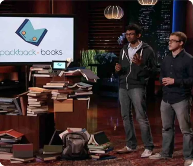 Packback co-founders Kasey Gandham and Mike Shannon pitching Packback Books on ABC's Shark Tank in 2014, surrounded by stacks of college textbooks.