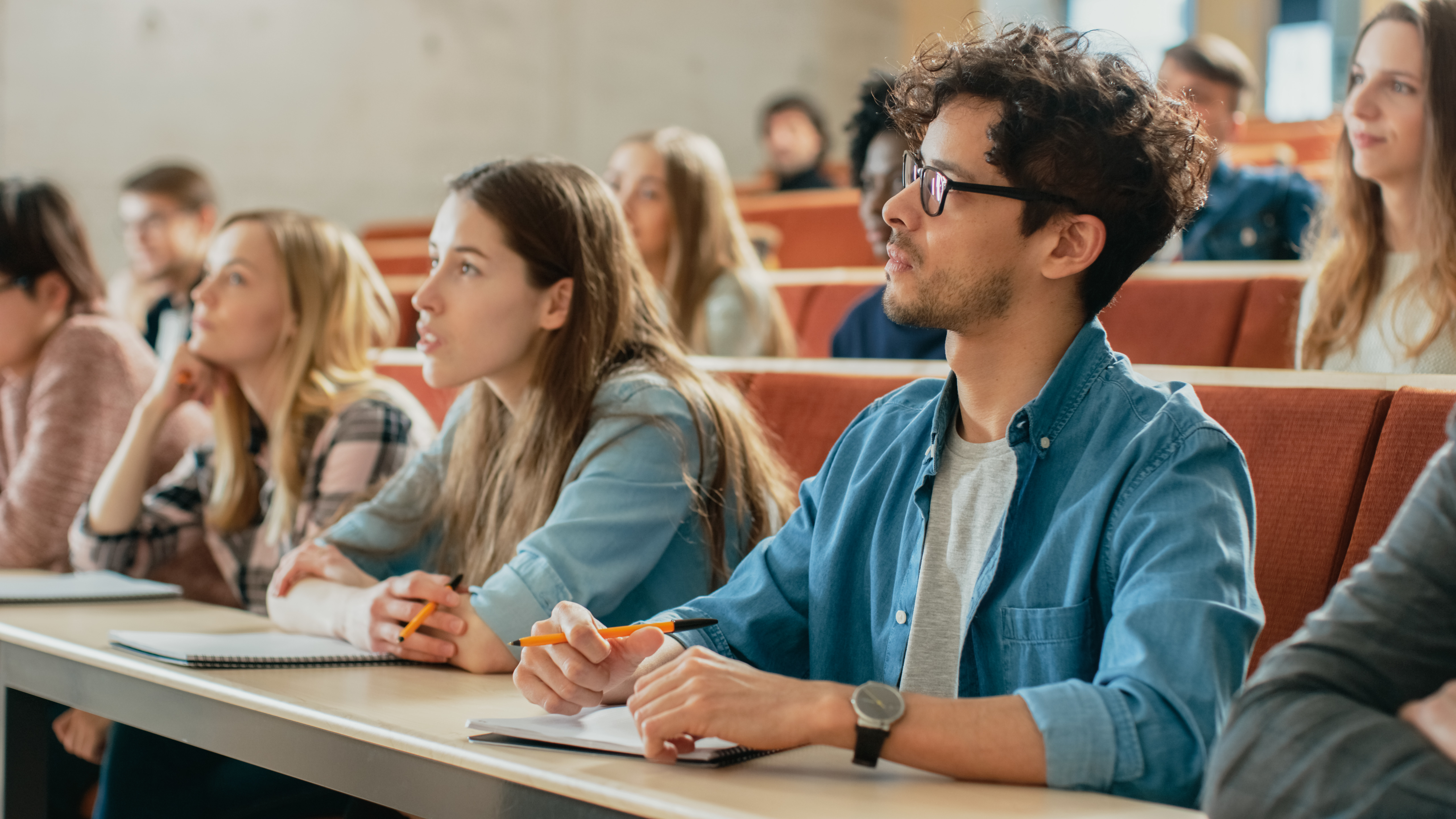 In the Classroom Multi Ethnic Students Listening to a Lecturer and Writing in Notebooks. Smart Young People Study at the College. In the Classroom Multi Ethnic Students Listening to a Lecturer and Writing in Notebooks. Smart Young People Study at the College.