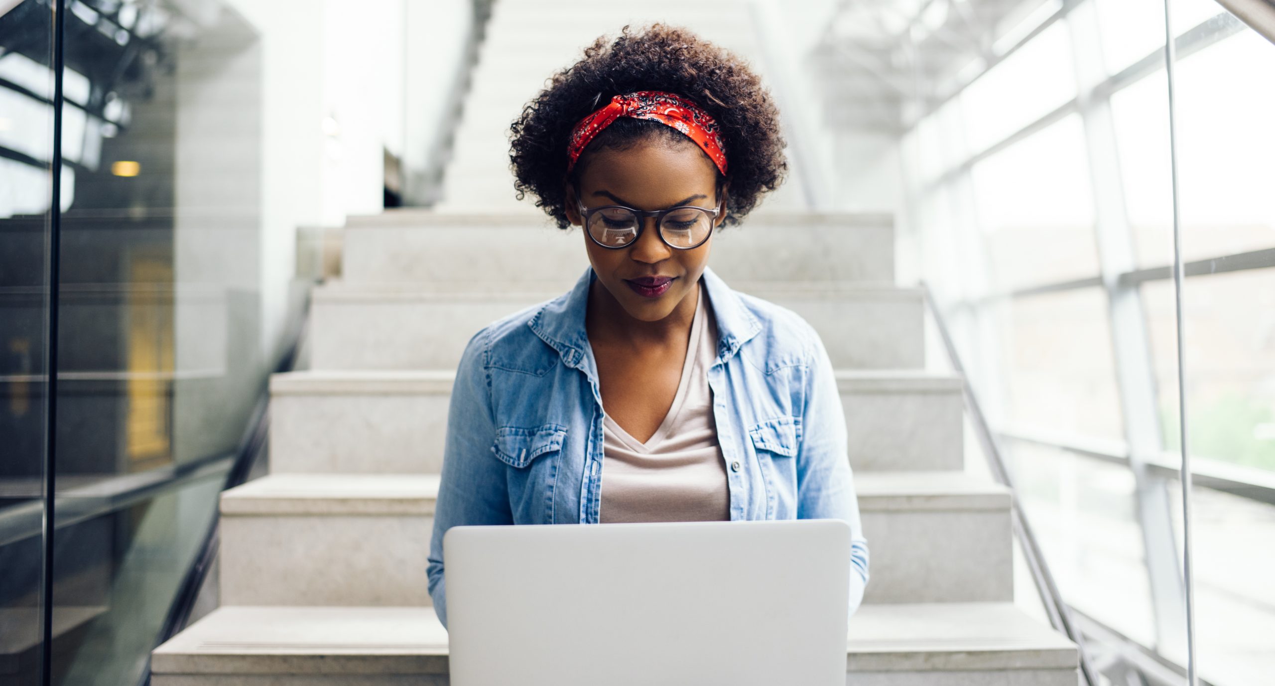 Focused young African student sitting on stairs using a laptop Focused young African female college student working on a laptop on some stairs on campus preparing for an exam
